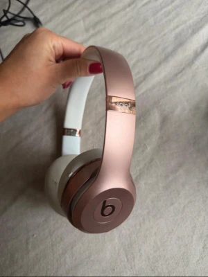 Beats Solo3 Wireless hörlurar roséguld - Kan hämtas från Helsingborg om du vill inte betala leverans frakt👍 Snygga Beats Solo3 Wireless hörlurar i roséguld med vita öronkuddar. De har en stilren design med metallic-finish och vadderad bygel för extra komfort. Trådlös anslutning och ikonisk Beats-logga på kåporna. Perfekta för musik och podcasts.