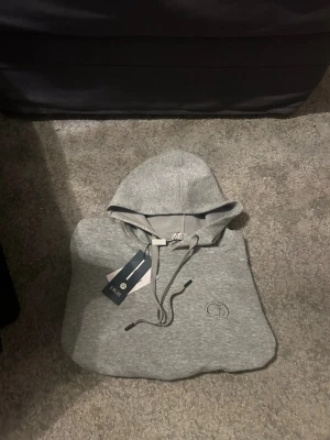 Grå hoodie från CD - Snygg grå hoodie från CD justerbar dragsko i huvan och diskret CD-logga broderad på bröstet. Tillverkad i mjukt material som känns skönt mot huden. Perfekt för dig som vill ha en stilren och exklusiv look.