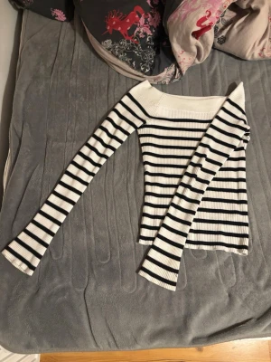 Randig off shoulder tröja från BikBok - Säljer en ribbad off shoulder tröja med svartvita horisontella ränder. Tröjan har långa ärmar och en bred urringning som sitter snyggt över axlarna. Perfekt för dig som gillar en stilren och trendig look.