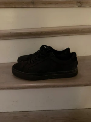 Helvita låga sneakers i skinn - Säljer ett par helsvarta sneakers med lågt skaft och klassisk design. Skorna har svarta skosnören och en diskret sula. Tillverkade i skinn för en stilren look som passar till det mesta.