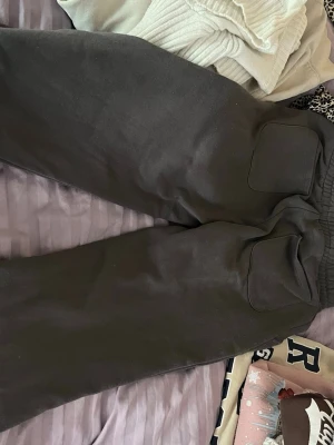 Mörkgrå mjukisbyxor med fickor - Säljer ett par mörkgrå mjukisbyxor med bred resår i midjan och två stora fickor framtill. Byxorna är gjorda i mjukt och bekvämt material, perfekta för chill dagar. Passar dig som gillar en avslappnad och enkel stil.