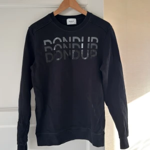 Svart sweatshirt från Dondup - Cool svart sweatshirt från Dondup med glansig logga tryckt framtill. Klassisk rund halsringning och långa ärmar. Tillverkad i mjukt material som känns skönt mot huden. Perfekt för en avslappnad och trendig look. Mitt pris: 700 kr 