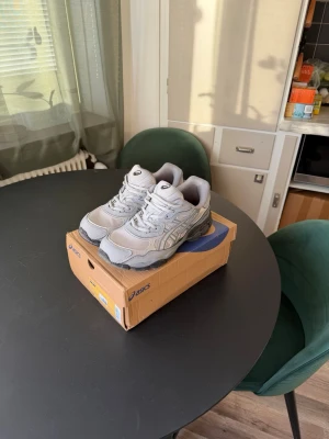 Gråa Asics sneakers - Säljer ett par gråa Asics sneakers med klassisk siluett och detaljer i mesh och syntet. Skorna har en chunky sula och reflekterande detaljer på sidan. Perfekta för dig som gillar sportig och clean stil.