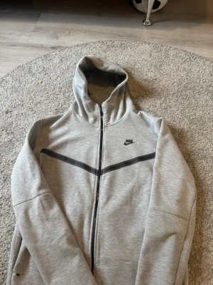 Grå Nike hoodie med dragkedja - Snygg grå hoodie från Nike med hel dragkedja och svart detalj över bröstet. XL fast passar L och M 