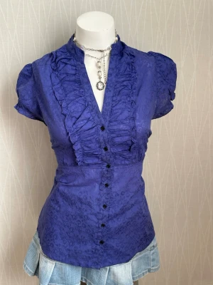 Coquette lila  blus med volang och knappar - Has some defects shown in the pictures. The tag says L, but it fits more like an M. The colour is more like purple in the reality