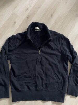 Svart halvzip tröja från COS - Svart tröja från COS i relaxed fit med halv dragkedja framtill och hög krage. Tillverkad i mjukt bomullsmaterial och har långa ärmar samt breda muddar vid ärmslut och nederkant. Enkel och stilren design som funkar till det mesta.