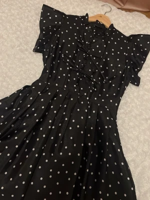 Polka kortärmad midjad långklänning  - Supersöt svart långklänning med vita prickar och snörningsdetaljer framtill. Klänningen har korta volangärmar. Kläningen är flowy och mycket skön, passar så bra för sommaren. 