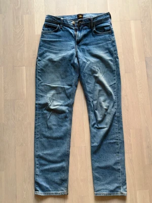 Ljusblå raka jeans från Lee - Säljer ett par klassiska blå jeans med rak passform från Lee. Jeansen har fem fickor och knappgylf. Materialet är slitstark denim bomull. En bältehälla är sönder. Storlek: W29 L32