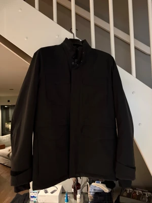 Svart jacka! från J.Lindeberg - Stilren svart jacka från J.Lindeberg med fyra fickor framtill och hög krage. Jackan har en minimalistisk design och diskret JL-logga på ärmen. Perfekt lager-på-lager-plagg för en modern look.