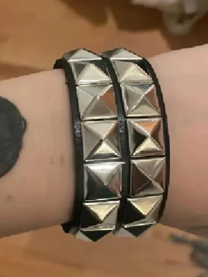 Svart nitarmlband med dubbla rader - Snyggt svart armband med dubbla rader av stora, fyrkantiga silverfärgade nitar. Armbandet har en rockig vibe och är gjort i konstläder med metallnitar som ger en cool och edgy look. Perfekt accessoar för att lyfta din outfit.