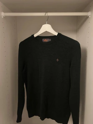 Mörkgrå stickad tröja från Morris - Snygg mörkgrå stickad tröja från Morris med rund halsringning och diskret broderad logga i lila på bröstet. Tröjan har långa ärmar och är tillverkad i mjukt material som passar perfekt till lager-på-lager-stil.