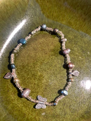 Pärlarmband med fjäril och löv handgjort stretch 18 cm  - Unikt armband med små glaspärlor i beige och oregelbundna sötvattenspärlor i olika färger. Armbandet har detaljer i form av metallberlocker, bland annat en fjäril och små löv. Perfekt för dig som gillar boho och personliga accessoarer.