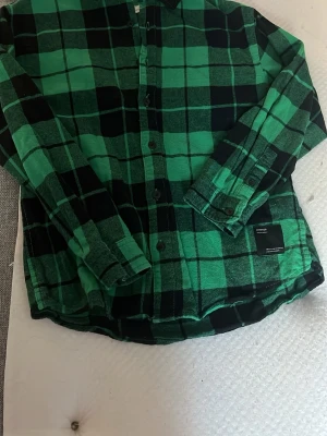 Grön och svart rutig skjorta från Zara - Snygg grön och svart rutig skjorta från Zara med klassisk krage och knäppning framtill. Skjortan har långa ärmar och är tillverkad i mjuk bomull, perfekt för en avslappnad stil.