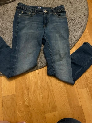 Blå jeans från Jack & Jones - Snygga blå jeans från Jack & Jones med klassisk femficksdesign och raka ben. Jeansen har en mellanblå tvätt med lätt slitningar och är tillverkade i ett mjukt denimtyg. Perfekta för en avslappnad och trendig stil.