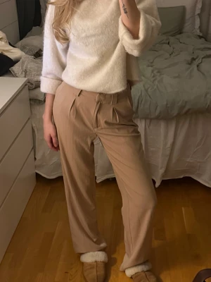Beige kostymbyxa från NA-KD - Snygga beige kostymbyxor från NA-KD med pressveck. Byxorna har vida ben och diskreta ränder i tyget för en stilren look. mjukt och följsamt tyg