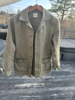 Overshirt John Henric - Stilren olivgrön overshirt från John Henric i bomull. Klassisk krage, tre utanpåliggande fickor och knäppning med bruna knappar. Perfekt lager-på-lager-plagg med avslappnad passform och snygga detaljer.