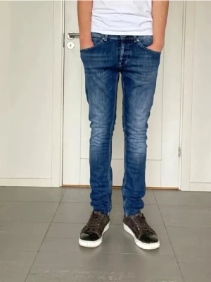 Dondup George  - Säljer ett par blå slim fit jeans ifrån Dondup med klassisk femficksdesign och snygga slitningar. Jeansen har normal midja och smal passform hela vägen ner. Perfekta till vardagslooken och passar till det mesta. Materialet är denim i bomull.