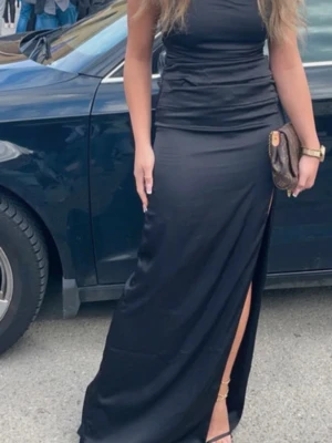 Svart långklänning med slits - Snygg svart långklänning med figurnära passform och hög slits på ena sidan. Klänningen är ärmlös och har en stilren, enkel design som ger en elegant look. Perfekt för dig som vill sticka ut med en klassisk och tidlös stil. Använd en gång.