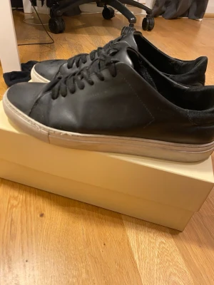 Svarta arigato skor clean 90 - Stilrena svarta arigato sneakers i läder med vita, tjocka sulor och svarta skosnören. Klassisk låg modell med enkel design som passar till det mesta. Perfekta för dig som gillar en clean och tidlös look.