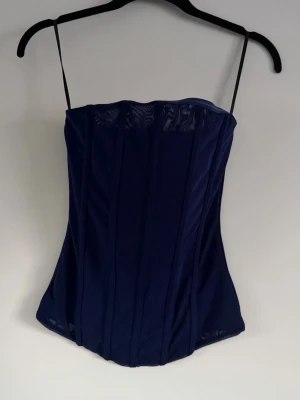 Mörkblå mesh korsett - Snygg mörkblå korsettopp i mesh. Toppen har en figurnära passform och transparenta detaljer upptill och nedtill för en trendig look.