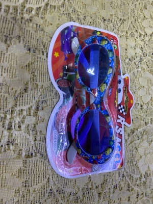 Blå Cars solglasögon barn - Säljer ett par blå solglasögon för barn med motiv från Disney Cars. Glasögonen har runda linser med blå ton och bågar dekorerade med färgglada figurer från filmen. Perfekta för dig som gillar bilar och vill ha en lekfull stil i solen.