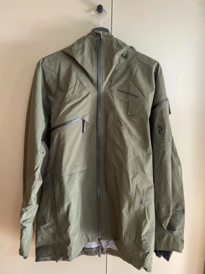 Olivgrön skaljacka Peak Performance - Få liv i min skaljacka som blivit för liten!  En fin mörkgrön skaljacka i Gore-Tex, egentligen herrmodell så passar både herr och dam!  I storlek S. Använd väldigt lite, inga skador.