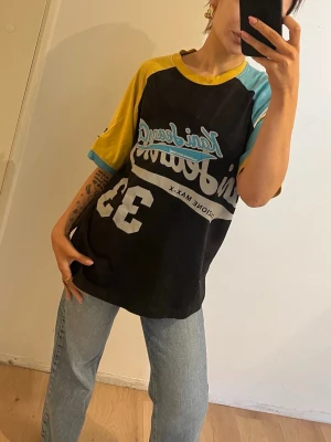 Vintage Kani Jeans Co. färgstark t-shirt - Säljer en vintage t-shirt från Kani Jeans Co från 90 talet.  med svart bas, gula och turkosa ärmar samt tryck i vitt och blått framtill. Oversized passform och sportig vibe med nummer 33 på framsidan. Perfekt för dig som gillar streetwear och färg. Storlek xl usa men passar mig som är xs beroende på passform 