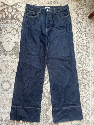 Mörkblå raka jeans med breda ben - Snygga mörkblå jeans med raka, breda ben och klassisk femficksdesign. Jeansen har hög midja och tydliga sömmar vid benslutet för en cool detalj. Perfekta för dig som gillar en avslappnad och trendig look.