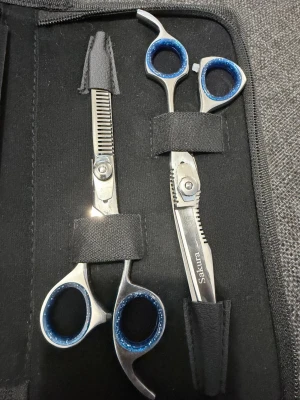 Sakura frisörsaxar i svart fodral - Säljer ett set med två professionella frisörsaxar från Sakura i ett stilrent svart fodral. Saxarna har blå detaljer i handtagen och är tillverkade i rostfritt stål. Perfekt för dig som vill fixa frisyren hemma eller på salong.
