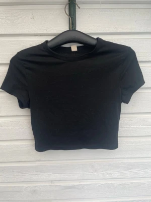 Svart croppad topp från SHEIN - En svart croppad topp från SHEIN Teen. T-shirten har korta ärmar, rund halsringning och är tillverkad i mjuk bomull. Enkel och stilren modell som passar perfekt till jeans eller kjol.