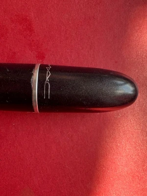 MAC mörkrött läppstift velvet teddy matte617 - Snyggt mörkrött läppstift från MAC i klassisk svart hylsa med silverdetaljer. Läppstiftet har en matt finish och den ikoniska MAC-loggan på hylsan. Perfekt för dig som vill ha en djup, intensiv färg på läpparna.