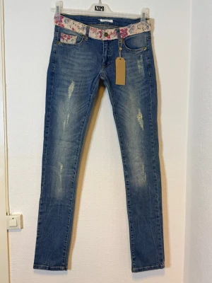 Blå skinny jeans med blommigt bälte - Midjan 40  cm  Längd 108  cm  Benvidd 25  cm 