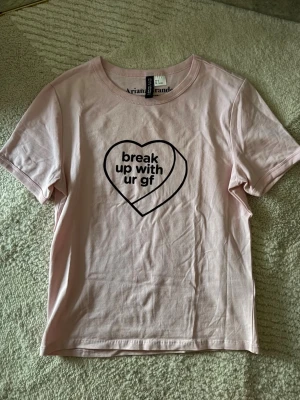 H&M rosa Ariana Grande t-shirt - Ljusrosa t-shirt i storlek S från H&M Ariana Grande med tryck i form av ett hjärta och texten 'break up with ur gf' på bröstet. Klassisk rund halsringning och korta ärmar. Sparsamt använd och säljer för kommer inte till nytta