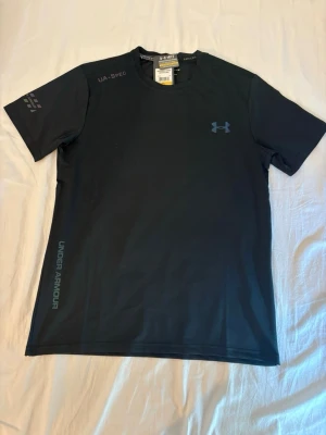Under Armour T-shirt - M men passar S - Säljer en stilren och funktionell tränings-T-shirt från Under Armour. Tillverkad i ett lätt och snabbtorkande material som håller dig sval och bekväm under träning. Perfekt för gym, löpning, padel eller vardagsbruk.  ✔️ Storlek: M ✔️ Skick: Helt ny med prislappar kvar ✔️ Färg: Svart ✔️ Lätt, ventilerande och fukttransporterande material  Hör gärna av dig om du har frågor eller vill ha fler bilder!