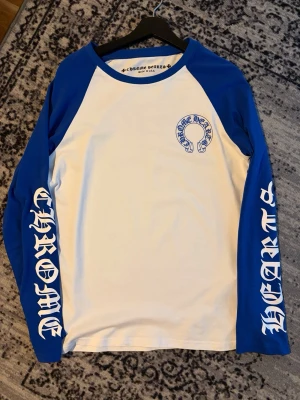 Chrome Hearts longsleeve - Snygg långärmad t-shirt från Chrome Hearts med blå ärmar och vit kropp. Stora tryck på båda ärmarna och ett klassiskt Chrome Hearts-tryck på bröstet. Perfekt för dig som gillar streetwear och vill sticka ut.