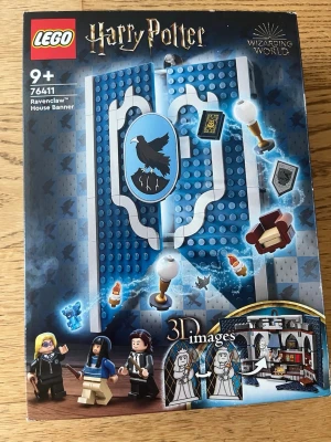 LEGO Harry Potter Ravenclaw Banner - Byggsats från LEGO Harry Potter-serien, modell 76411, Ravenclaw House Banner. Innehåller blå och grå byggklossar, minifigurer och tillbehör som skildrar Ravenclaws uppehållsrum. Setet har detaljerade tryck, 3D-effekter och flera små tillbehör. Perfekt för Harry Potter-fans.