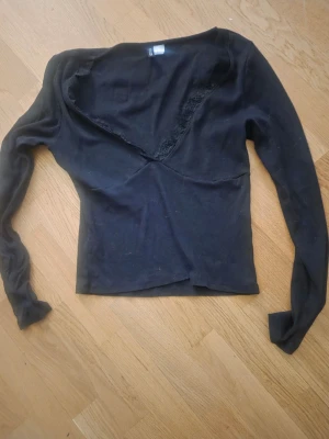 Svart långärmad topp med spets - Snygg svart långärmad topp från hm med djup ringning och dekorativ spetskant. Tillverkad i mjukt stretchigt material som sitter skönt på kroppen. Perfekt för dig som gillar en enkel men ändå detaljrik stil.
