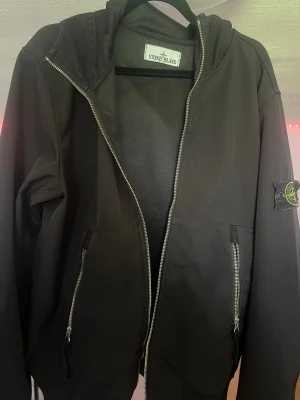 Bomberjacket Stone Island - Säljer en stilren och eftertraktad Stone Island bomberjacka med huva i storlek M. Jackan är använd men fortfarande i mycket bra skick, utan hål, fläckar eller märkbart slitage.  Jackan har QR-kod för äkthetsverifiering och den ikoniska Stone Island-designen som passar både till vardags och en mer uppklädd streetwear-look.  Den kan säljas som den är eller tvättas innan leverans enligt köparens önskemål