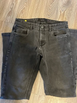 Svarta slim fit jeans från S.M.D - Snygga svarta slim fit jeans från S.M.D med klassisk femficksdesign och knappgylf. Jeansen har en tvättad look och raka ben. Perfekta för dig som gillar en stilren och enkel look. Materialet känns mjukt och stretchigt för extra komfort.