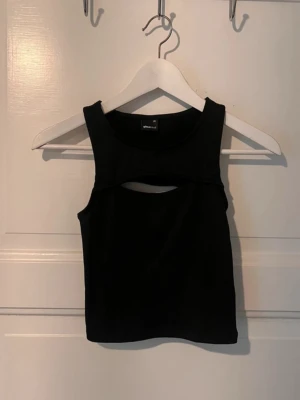 Svart croppad linnetopp med cut out - Säljer en svart croppad linnetopp från Gina Tricot med snygg cut out-detalj både fram och bak. Toppen är ärmlös och har en tight passform som framhäver figuren. Perfekt att styla med höga jeans eller kjol.