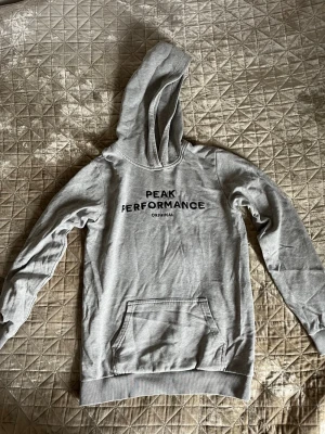 Grå hoodie från Peak Performance - Grå hoodie från Peak Performance med svart tryck på bröstet. 