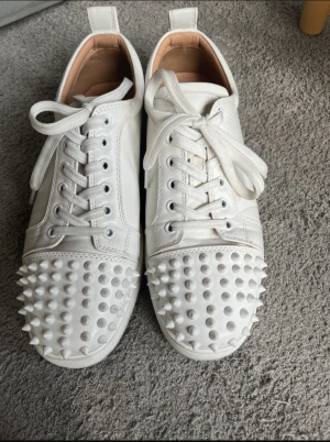Christian Louboutin vita sneakers med nitar - Säljer ett par vita sneakers från Christian Louboutin i skinn med ikonisk röd sula och coola nitar över tån. Nästan aldrig använda