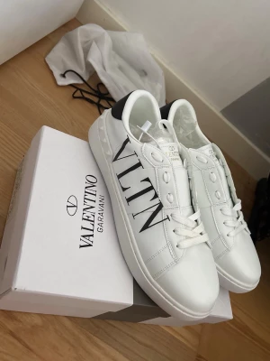 Valentino Garavani vita sneakers - Säljer ett par exklusiva Valentino Open sneakers i storlek 44 med den ikoniska VALENTINO-logotypen på sidan. Skorna är helt nya och i perfekt skick, utan några tecken på användning.  De säljs då de tyvärr inte passade mig i storleken. Ett utmärkt tillfälle att köpa ett par lyxiga sneakers i nyskick till ett förmånligt pris.  Ingår:  * Originalbox * Samtliga originaltillbehör  Skorna kombinerar hög komfort, förstklassiga material och en stilren design som passar både till vardag och mer uppklädda