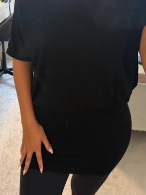 Svart offshoulder kortklänning - Snygg svart kortklänning med offshoulder-design och lös passform upptill. Klänningen har korta ärmar och är tillverkad i ett mjukt, stretchigt material som sitter bekvämt på kroppen. Perfekt för dig som gillar en enkel men trendig look.