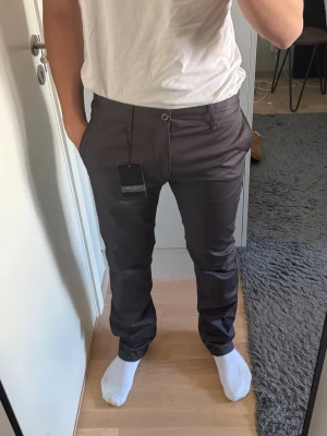 Mörkbruna kostymbyxor från Zara  - Slimmade mörkbruna kostymbyxor från Zara Selected Homme med klassisk passform, hällor för bälte och sidofickor. Byxorna har en stilren look och är tillverkade i ett mjukt, vävt material som ger en dressad känsla. Hölt oanvänd och nya med lapp kvar.