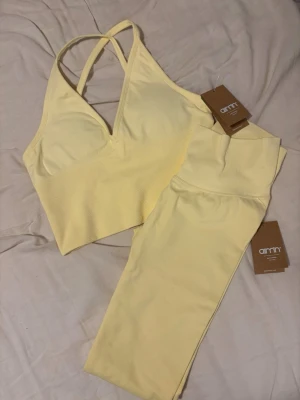 Gult sömlöst träningsset Aim'n - Fräscht gult träningsset från Aim'n med sport-bh och matchande tights. Bh:n har smala axelband och v-ringning, medan tightsen har hög midja och sömlös design. Tillverkat i stretchigt material som ger skön passform och rörelsefrihet. Perfekt för gym, yoga eller löpning.