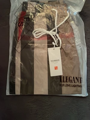 Bubbrye shorts för sommaren väldigt sköna och snygga - Säljer ett par snygga shorts från  med breda vertikala ränder i svart, beige, grått och rött. Shortsen har elastisk midja med vit snörning och sidofickor. Perfekta för sommaren och har en modern, avslappnad stil.