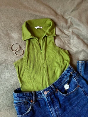 Grön ärmlös polotopp - Snygg chartreuse ribbad polotopp från Envii med dragkedja framtill och hög krage. Toppen är ärmlös och har en svagt croppad passform (precis till naveln) som passar perfekt till jeans eller kjol. Materialet är mjukt och det går att ställa in hur mycket ringing du vill visa genom dragkedjan 🍏