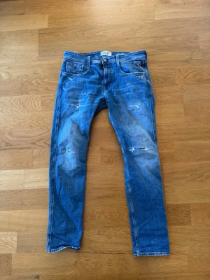 Replay Anbass  - Säljer ett par blå jeans med raka ben och slitna detaljer på framsidan ifrån replay. Jeansen är 33/32 och har mycke bra skick.