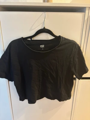 Svart croppad t-shirt från 157 - En svart croppad t-shirt från 157 med rund halsringning och korta ärmar. Enkel och stilren design i mjuk bomull, perfekt att matcha med jeans eller kjol för en avslappnad look.